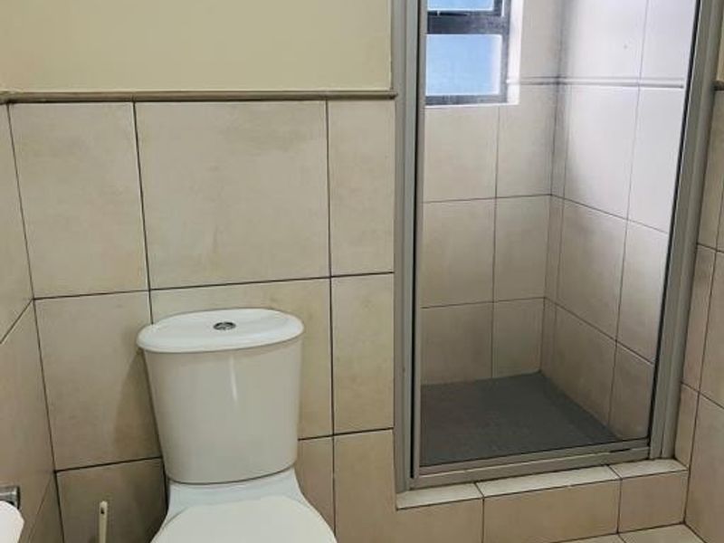 A functional bathroom featuring a standard toilet and a glass-enclosed shower with neutral wall and floor tiling.
