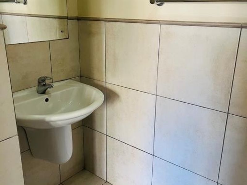 A compact bathroom featuring a pedestal basin, chrome fixtures, and neutral ceramic tiling throughout.