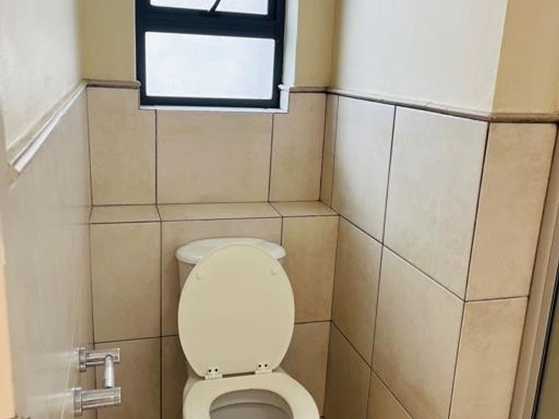 A compact bathroom featuring neutral wall and floor tiles, a standard toilet, and a top-hung window for natural light and ventilation.
