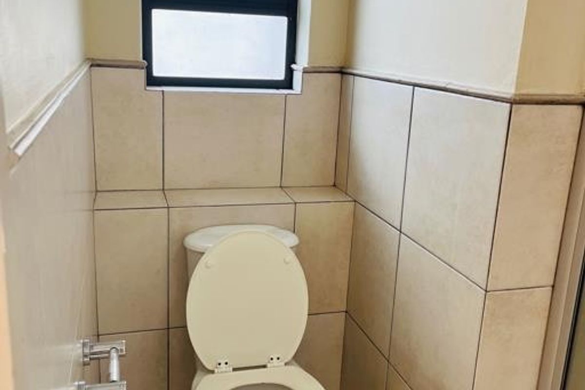 A compact bathroom featuring neutral wall and floor tiles, a standard toilet, and a top-hung window for natural light and ventilation.