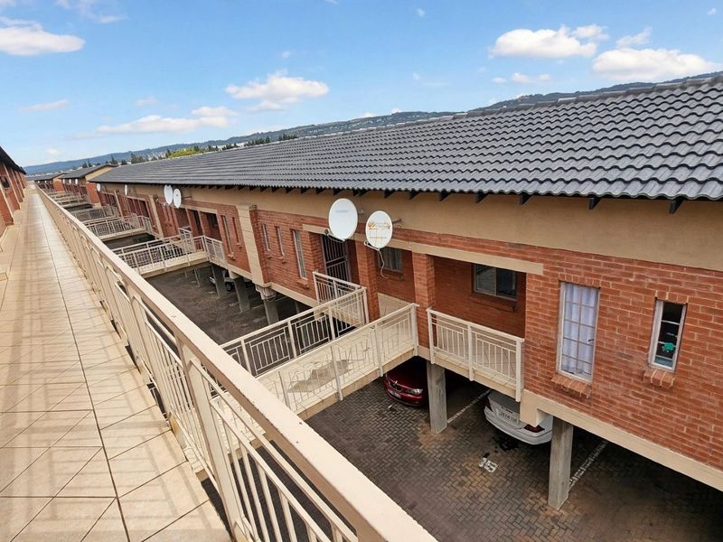 An elevated view of the apartment complex exterior, featuring a tiled walkway, brick facade, and covered parking area below.