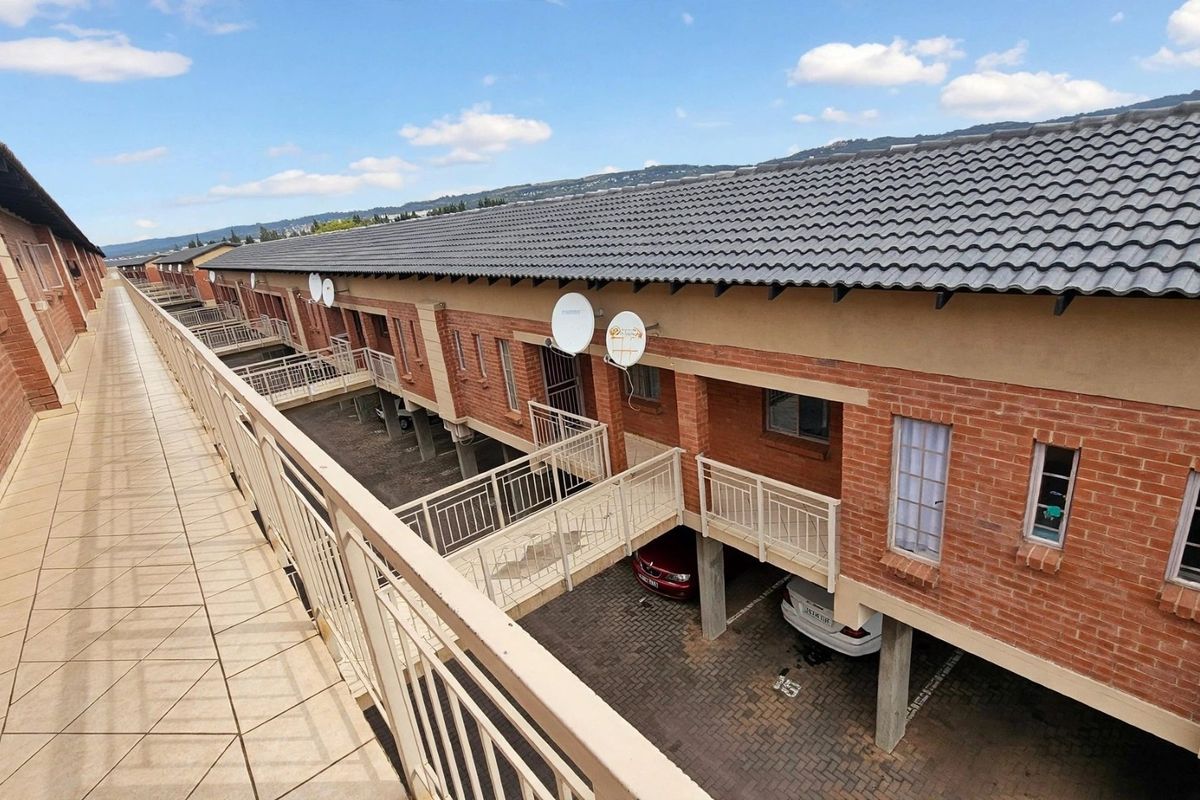 An elevated view of the apartment complex exterior, featuring a tiled walkway, brick facade, and covered parking area below.