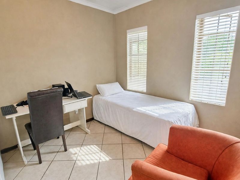 A functional bedroom featuring tiled flooring, neutral wall finishes, and dual windows fitted with venetian blinds.