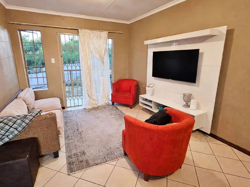 A living room featuring tiled flooring, a built-in media unit, and a sliding door with a security gate leading to the exterior.