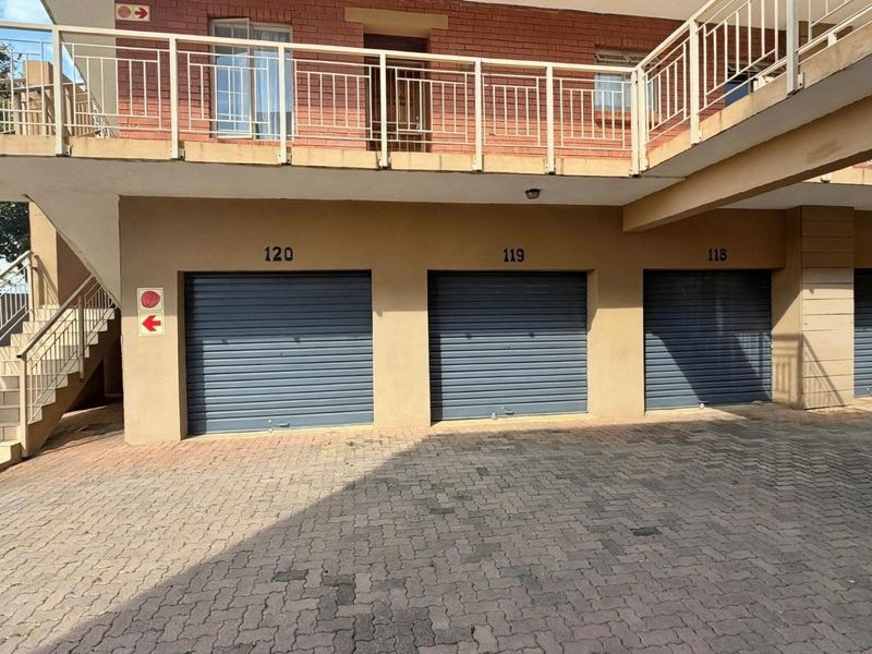 A row of numbered garage units with roller shutter doors, featuring a paved driveway and an external staircase leading to the upper level.