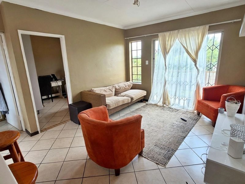 A living room featuring tiled flooring and a sliding glass door with security gate, providing access to the exterior.