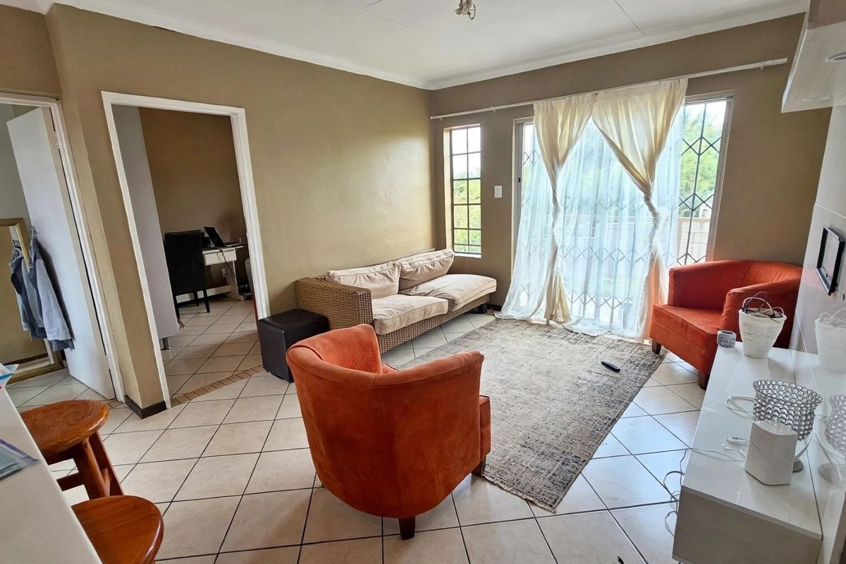 A living room featuring tiled flooring and a sliding glass door with security gate, providing access to the exterior.