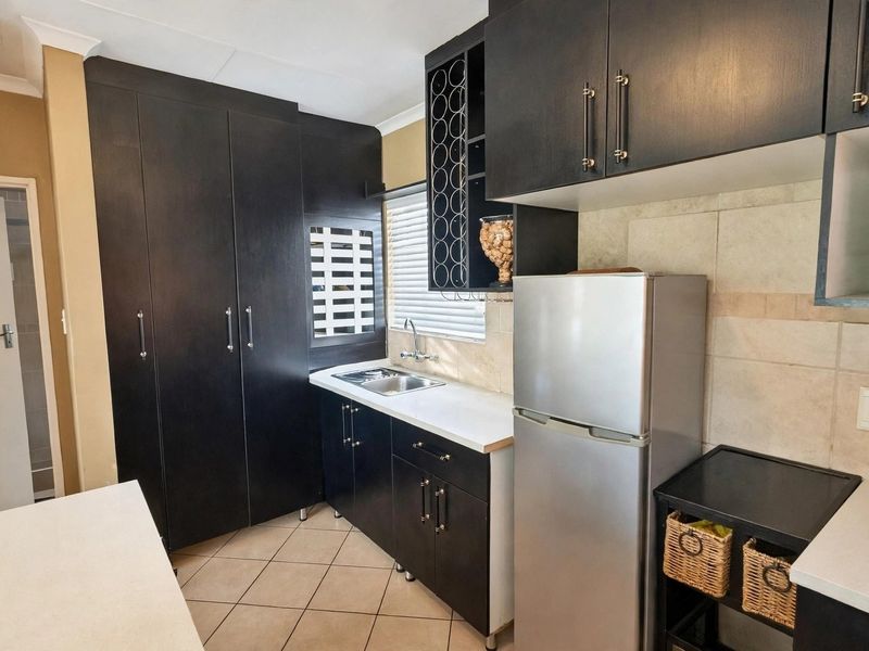 Compact kitchen featuring dark wood cabinetry, integrated wine storage, stainless steel sink, and neutral tiled backsplash and flooring.