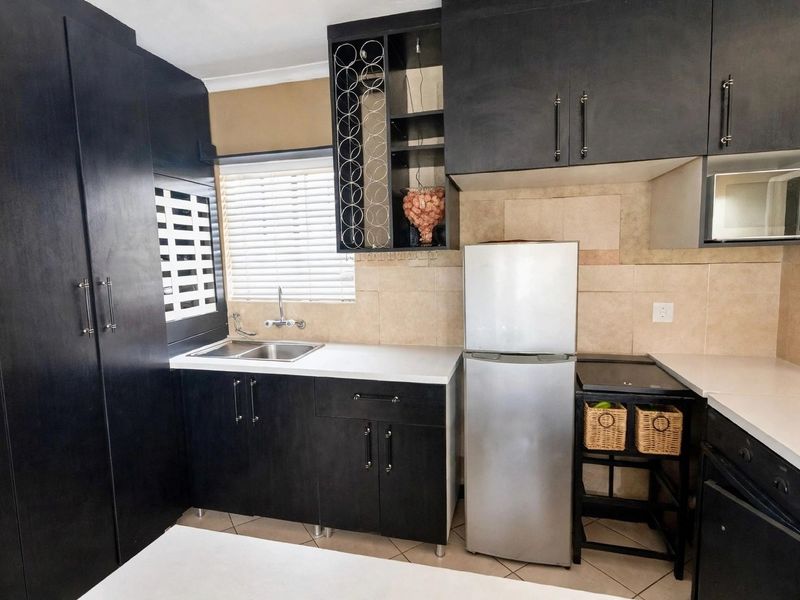 A compact kitchen featuring dark cabinetry, a double sink, tiled backsplash, and built-in microwave, offering functional storage and preparation space.
