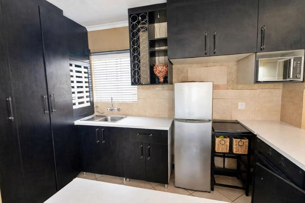 A compact kitchen featuring dark cabinetry, a double sink, tiled backsplash, and built-in microwave, offering functional storage and preparation space.