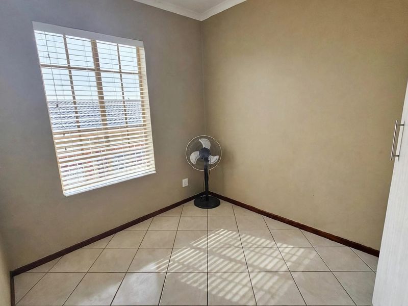 A bright, empty bedroom featuring neutral wall tones, tiled flooring, and a built-in cupboard, offering a clean canvas for personalization.