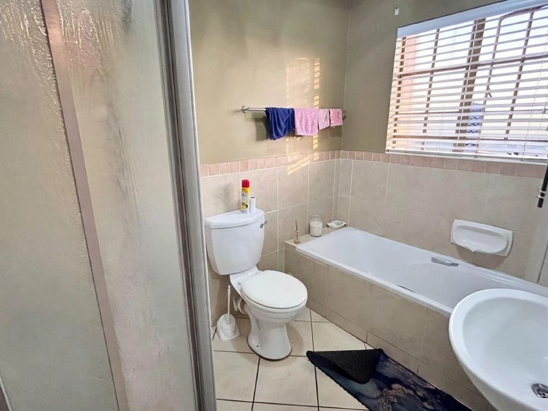A functional bathroom featuring a bathtub, pedestal basin, toilet, and a separate shower enclosure with neutral wall and floor tiling.