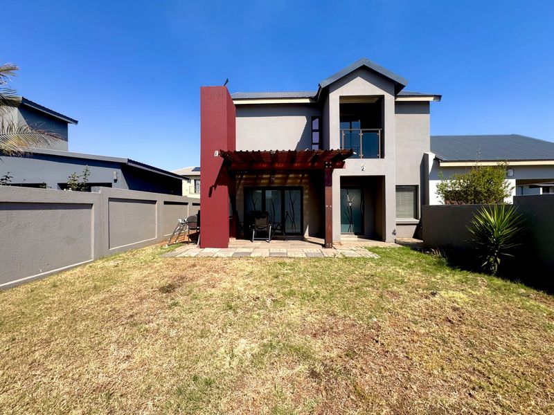 Rear view of the house featuring a paved patio with a wooden pergola, a balcony, and a private garden enclosed by boundary walls.