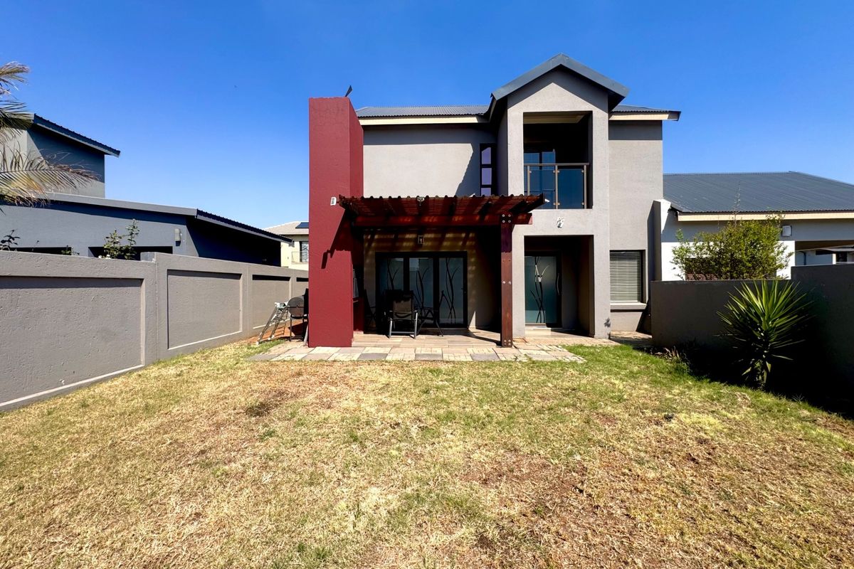 Rear view of the house featuring a paved patio with a wooden pergola, a balcony, and a private garden enclosed by boundary walls.