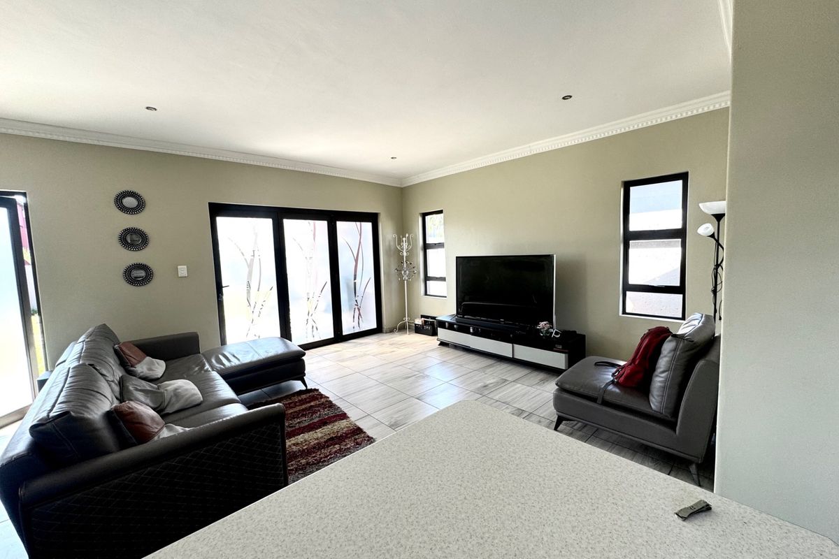Spacious living room featuring tiled flooring, modern cornicing, recessed lighting, and large aluminium-framed sliding doors providing access to the exterior.