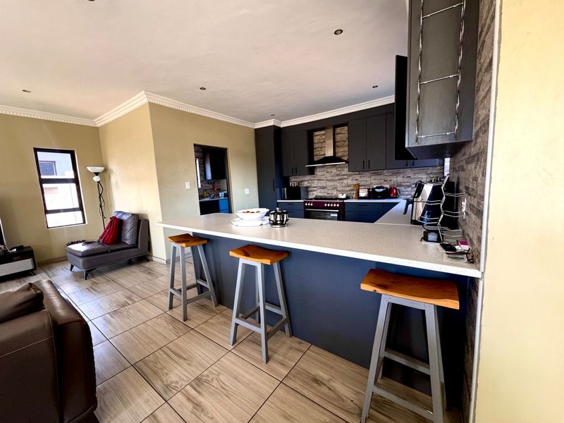 Open-plan kitchen and living area featuring a central island, modern dark cabinetry, built-in appliances, and tiled flooring throughout.