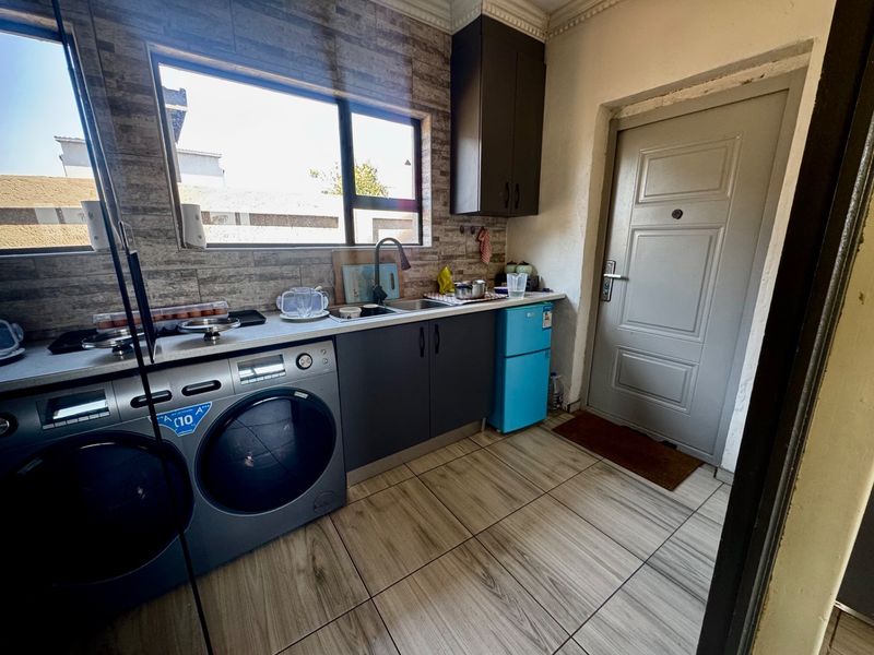 A functional laundry area featuring built-in cabinetry, a stainless steel sink, tiled flooring, and direct access to an exterior door.