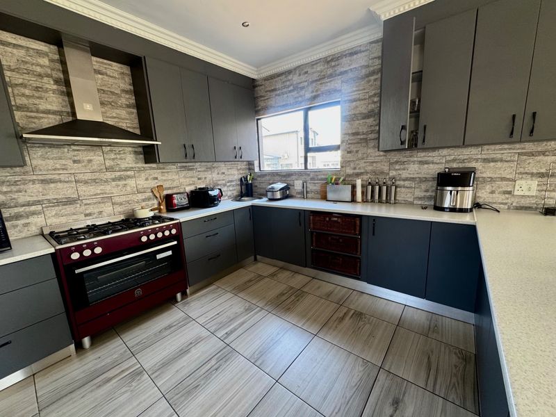 Modern kitchen featuring dark grey cabinetry, stone countertops, a gas stove with extractor fan, and wood-look tiled flooring.