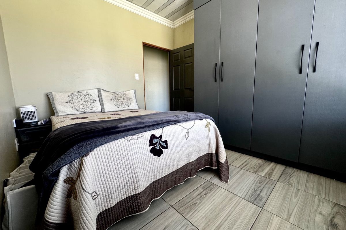 A bedroom featuring modern grey built-in cupboards, wood-look tiled flooring, and a panelled ceiling with decorative cornice.