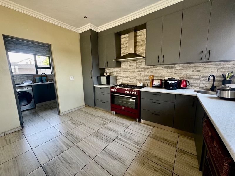 Modern kitchen featuring dark grey cabinetry, stone countertops, a red gas stove with extractor fan, and tiled flooring, with an adjacent scullery area.