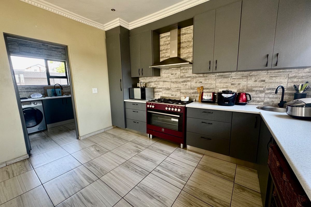 Modern kitchen featuring dark grey cabinetry, stone countertops, a red gas stove with extractor fan, and tiled flooring, with an adjacent scullery area.