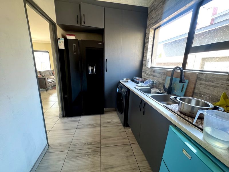 A functional scullery featuring modern dark cabinetry, a double sink, tiled backsplash, and tiled flooring, providing convenient additional prep and wash-up space.