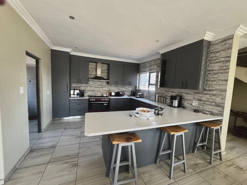 Modern kitchen featuring dark grey cabinetry, stone countertops, a central island with breakfast bar seating, and tiled flooring throughout.