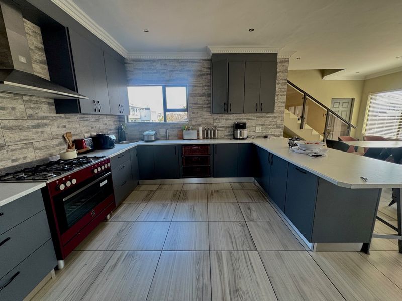 Modern kitchen featuring dark cabinetry, stone countertops, a gas stove with extractor fan, and tiled flooring, seamlessly integrated into an open-plan living space.