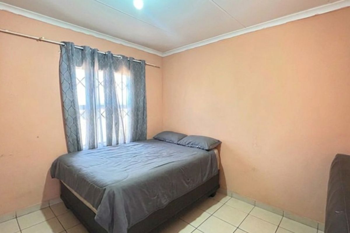 A simple bedroom featuring tiled flooring, security bars on the window, and plain wall finishes, offering a functional space ready for cosmetic updates.