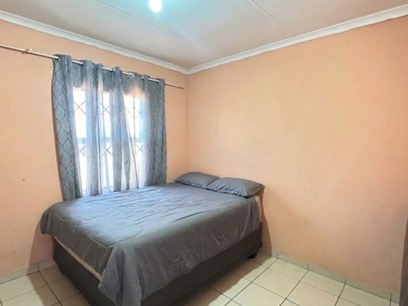 A simple bedroom featuring tiled flooring, security bars on the window, and plain wall finishes, offering a functional space ready for cosmetic updates.