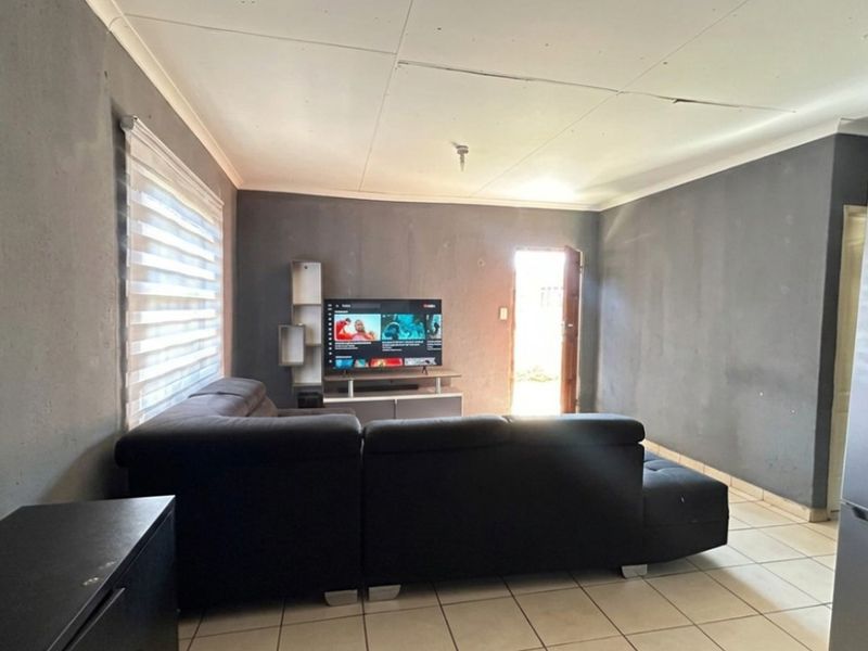A living room featuring tiled flooring, roller blinds, and ceiling cornice, currently showing signs of wear including visible ceiling cracks.