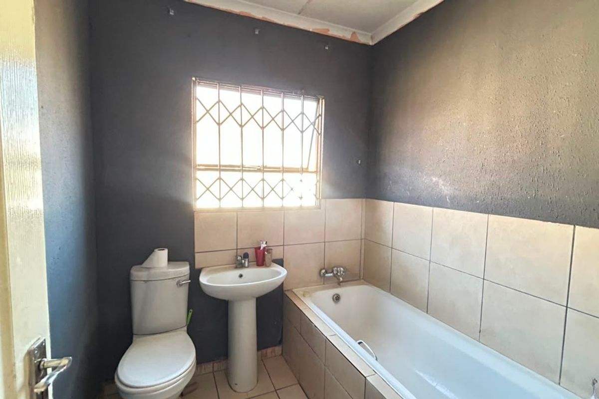 A functional bathroom featuring a pedestal basin, bathtub, and toilet, with security bars on the window and tiled wall sections.