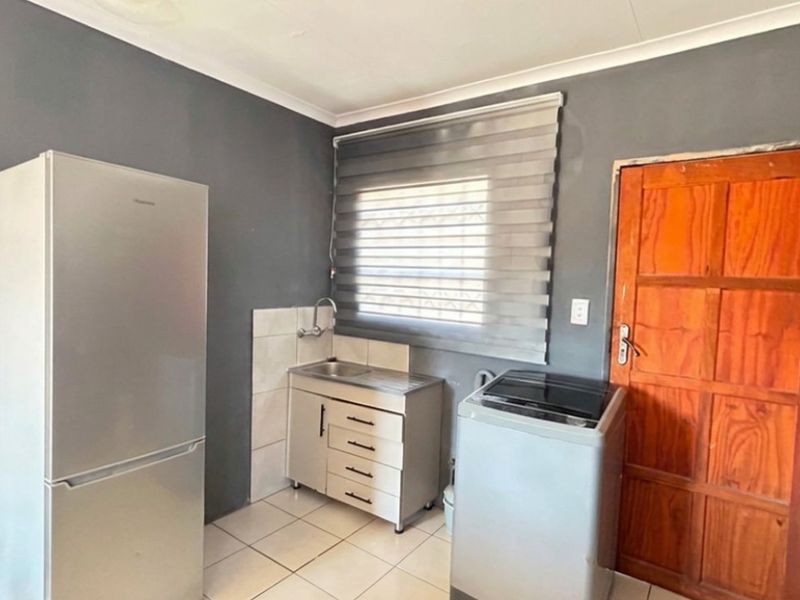 A functional laundry area featuring a stainless steel sink, tiled splashback, and tiled flooring, providing a practical space for household utility tasks.