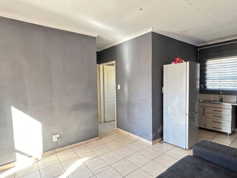 Open plan living and kitchen area featuring tiled flooring, built-in cabinetry, and roller blinds, requiring some cosmetic attention to walls and ceiling.