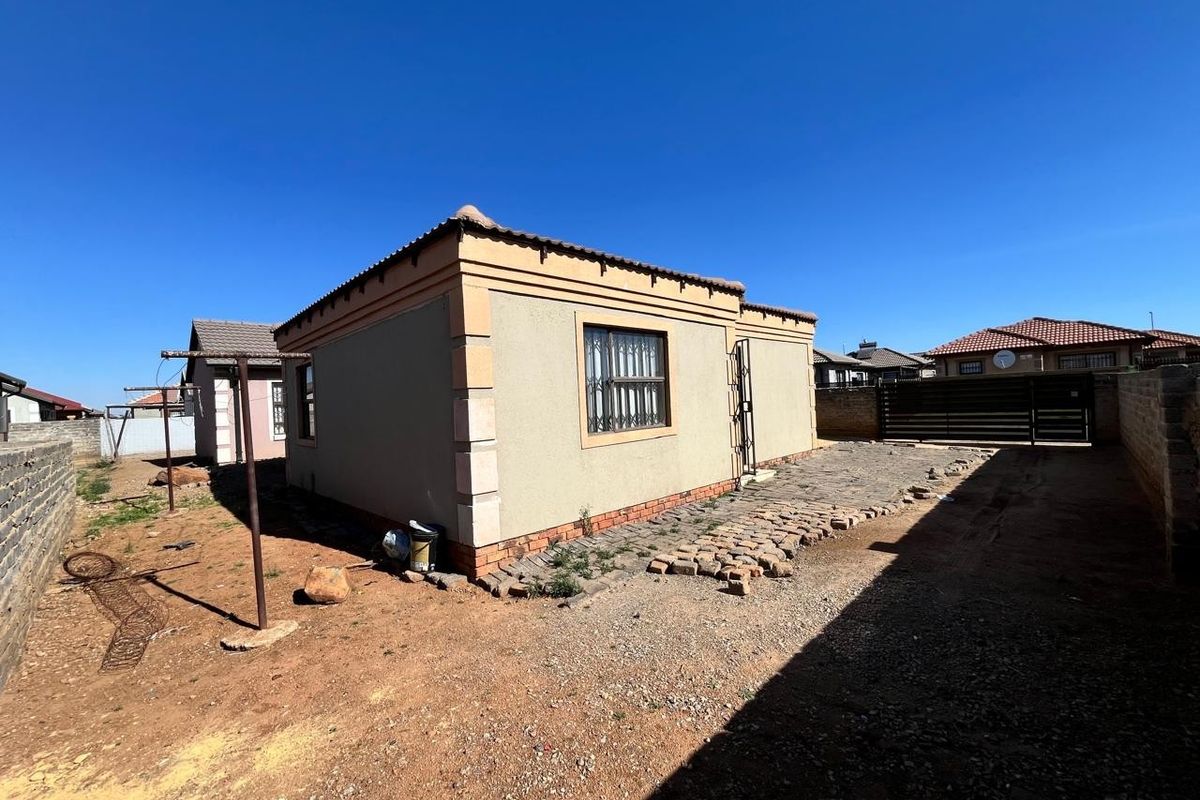 Rear view of the property featuring a paved area, security bars on windows, and a perimeter wall with a metal gate.