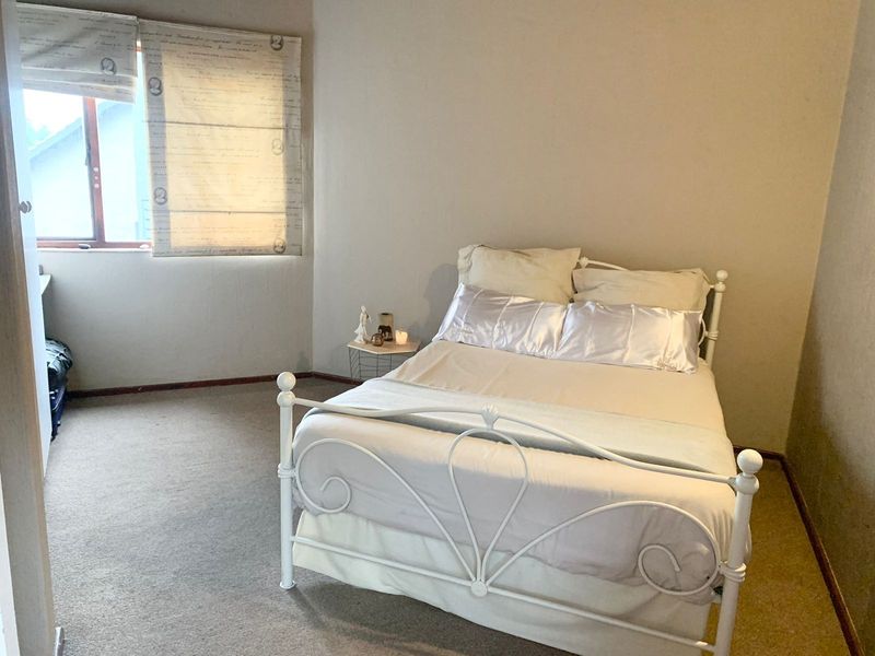 A standard bedroom featuring carpeted flooring and a window with fitted blinds.