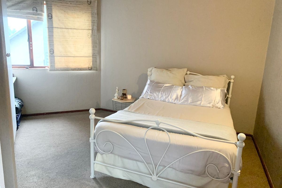 A standard bedroom featuring carpeted flooring and a window with fitted blinds.