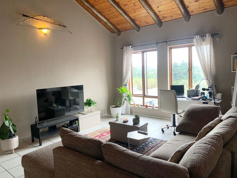 A comfortable living room featuring a vaulted timber beam ceiling, tiled floors, and large windows that provide ample natural light.