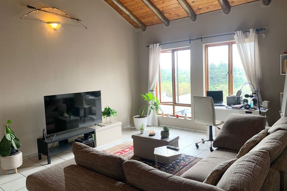 A comfortable living room featuring a vaulted timber beam ceiling, tiled floors, and large windows that provide ample natural light.