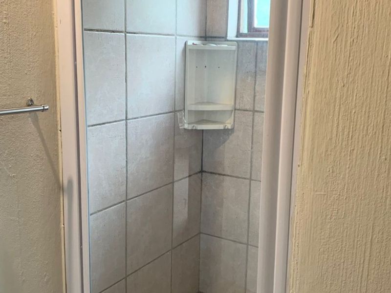 A compact shower stall featuring tiled walls, a pebble mosaic floor, and a built-in corner caddy, requiring maintenance and cosmetic updates.