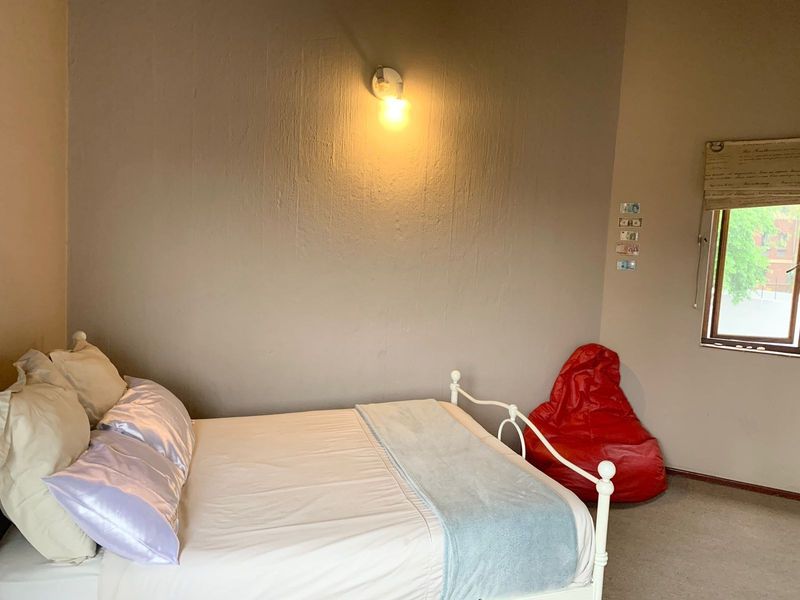 A bedroom featuring a wall-mounted light fixture and a window with a roller blind, providing a functional and simple living space.
