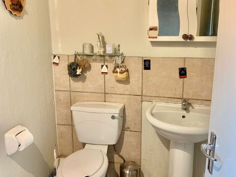 A compact bathroom featuring a pedestal washbasin, toilet, and wall-mounted medicine cabinet with neutral tiled splashbacks and flooring.