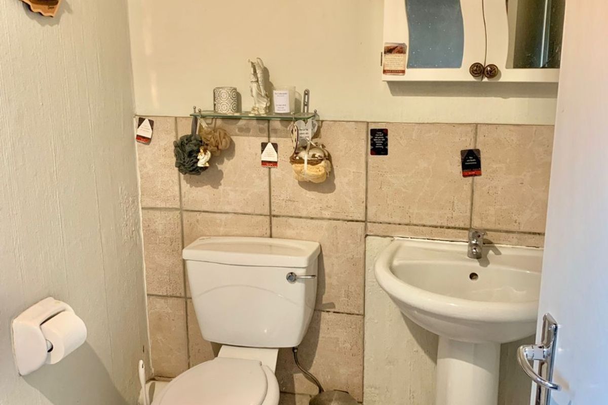 A compact bathroom featuring a pedestal washbasin, toilet, and wall-mounted medicine cabinet with neutral tiled splashbacks and flooring.