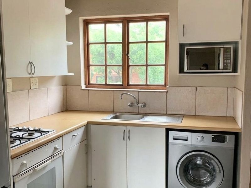 Compact kitchen featuring white cabinetry, laminate countertops, built-in oven and hob, tiled backsplash, and exposed timber ceiling beams.