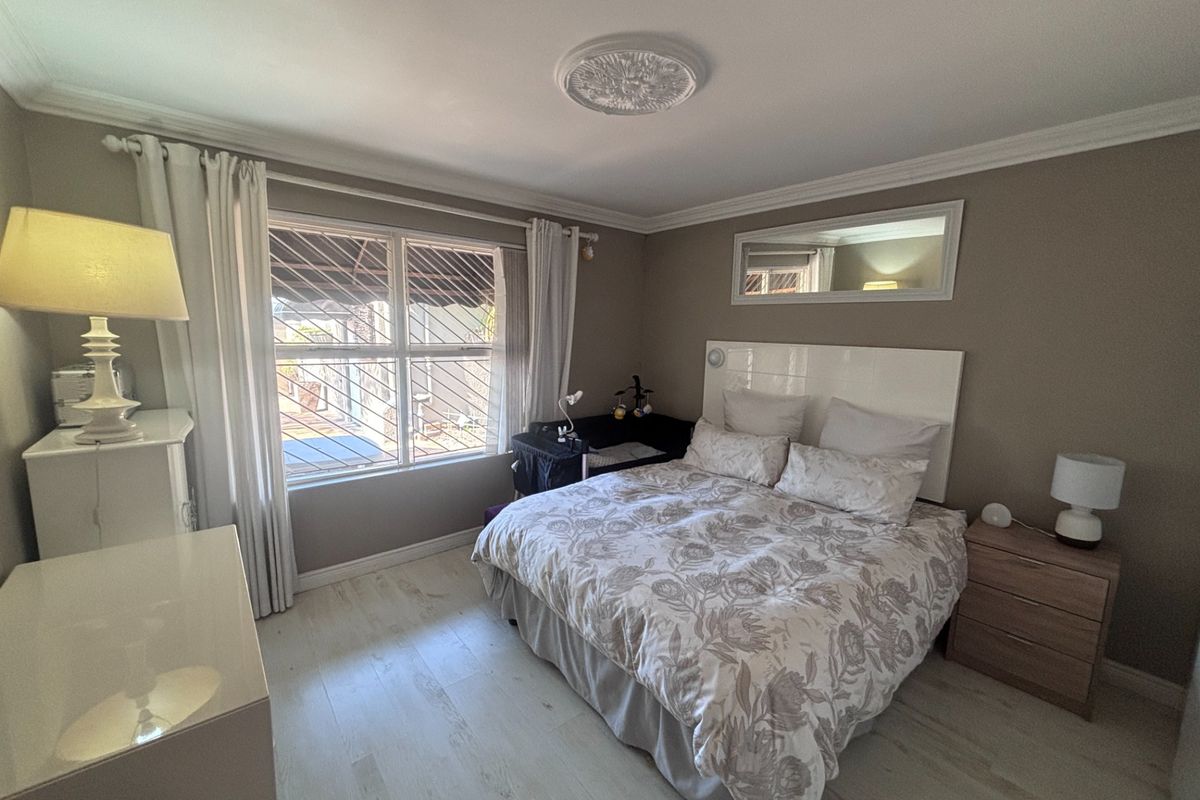 A well-maintained bedroom featuring light-toned laminate flooring, decorative ceiling rose, crown molding, and security bars on the windows.