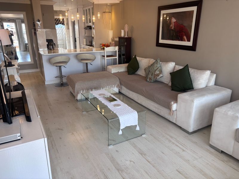 An open-plan living area featuring light laminate flooring, a modern kitchen with a breakfast bar, and elegant pendant lighting throughout the space.