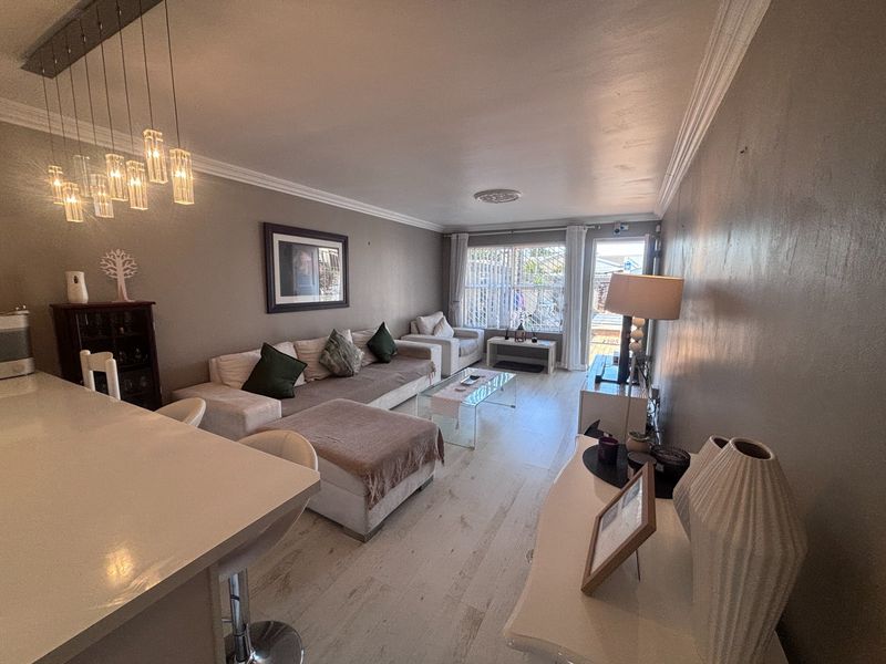 Open-plan living area featuring laminate flooring, crown molding, and modern pendant lighting, with direct access to an outdoor patio space.