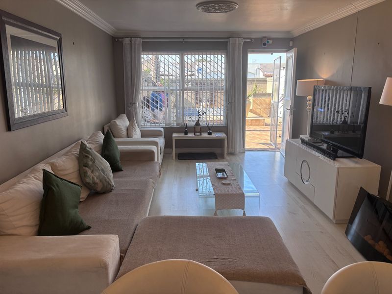 A well-lit living room featuring laminate flooring, crown molding, and direct access to an outdoor patio area through a glass door.