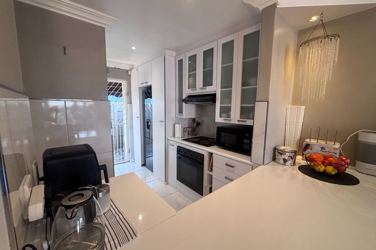 Modern kitchen featuring white cabinetry, quartz countertops, built-in oven and hob, and recessed lighting, leading to a rear access door.