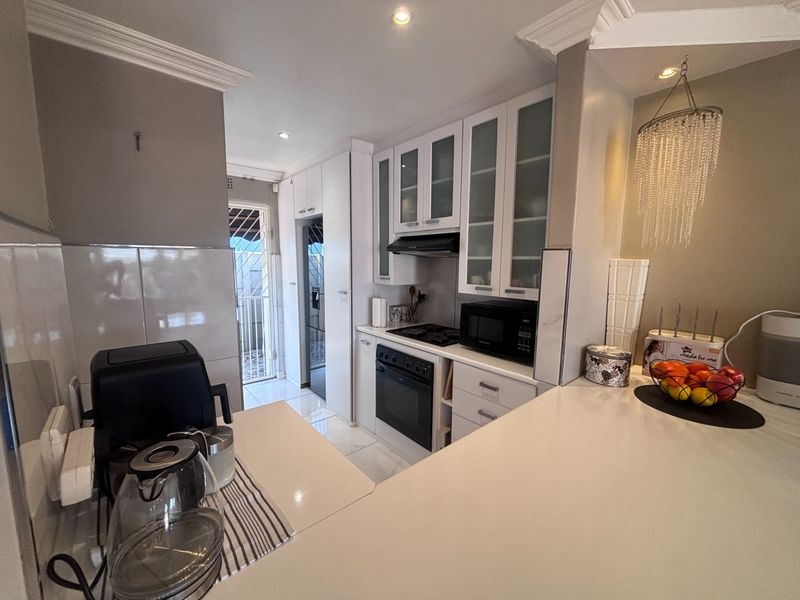 Modern kitchen featuring white cabinetry, quartz countertops, built-in oven and hob, and recessed lighting, leading to a rear access door.